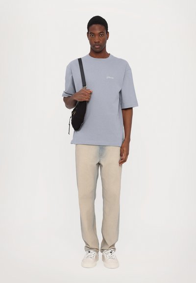 Light blue cotton T-shirt with short sleeves and a crew neck, paired with light beige jeans and white sneakers. Black shoulder bag included.