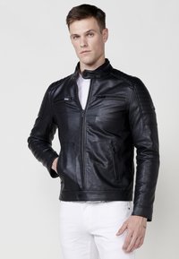 Giacca di pelle nera con vestibilità slim, colletto alto, zip frontale e dettagli delle tasche; presenta accenti a coste sulle spalle e texture liscia.