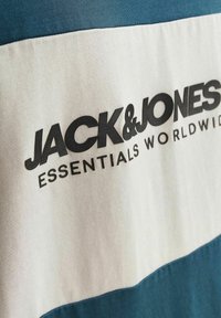 T-shirt i blå og hvid. Har et fedt sort logo: "JACK & JONES" og "ESSENTIALS WORLDWIDE." Fremstillet af blødt bomuldsstof.
