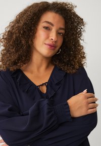 Marineblouse met gerimpelde halslijn en strikdetail, voorzien van lange, puffed mouwen met gerimpelde manchetten, gemaakt van lichtgewicht stof.