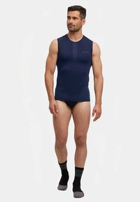 Marineblauw mouwloos bodyshirt met een gladde textuur, voorzien van een subtiel logo en een ronde halslijn, gecombineerd met zwart ondergoed en gestreepte sokken.