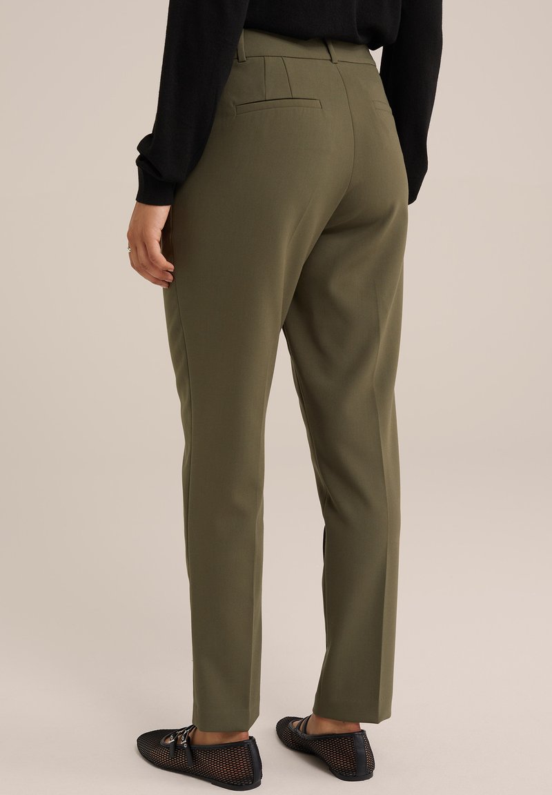 Olijfgroene op maat gemaakte broeken met rechte pijpen, voorzien van achterzakken en een gladde textuur, gecombineerd met zwarte mesh instapschoenen.