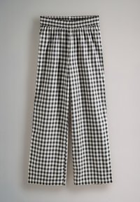 Mustvalge ruudulise mustriga laia säärega püksid, millel on elastne vöökoht, väljendades kootud kangast ja lõdva, vooluva kujuga.