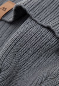 Tessuto grigio a maglia a coste con una texture liscia, caratterizzato da un orlo piegato e una piccola etichetta in pelle.