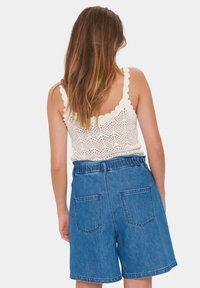Top croșetat bej deschis, cu margini ondulate, asortat cu pantaloni scurți din denim albastru, cu talie înaltă, brâu elastic și buzunare posteriori.