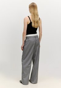 Graue weit geschnittene Hose mit Karomuster, versehen mit einem weißen Bund und Hintertaschen. Getragen mit einem schwarzen Tanktop.