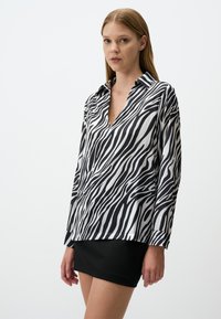 Blusa in seta con stampa a zebra bianco e nero, caratterizzata da scollatura a V, maniche lunghe e vestibilità aderente, abbinata a una mini gonna nera.