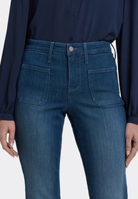 Mörkblå denimjeans med hög midja, sydda sömmar och två bakfickor. Tyget har en lätt textur och en hållbar design.