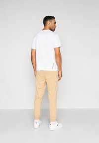 Fehér rövid ujjú póló bézs színű, szűkített szárú nadrággal, amely rugalmas derékpánttal és bordázott boka mandzsettával rendelkezik. A megjelenést fehér tornacipő egészíti ki.