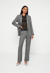 Szary, szyty na miarę garnitur z usztywnioną marynarką, dopasowanymi spodniami oraz prześwitującą czarną bluzką pod spodem. Do tego beżowe szpilki z szpiczastymi noskami.