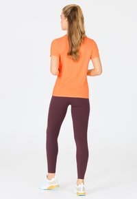 Orange kortärmad träningsöverdel ihop med mörklila leggings och vita sneakers med färgglada accenter, vilket ger en smal, tight silhuett.