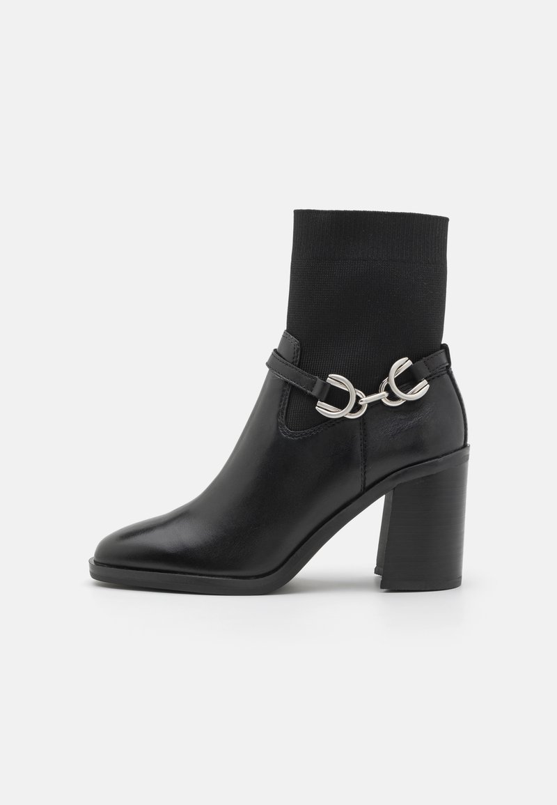 Stivale nero alla caviglia con tacco robusto, corpo in pelle liscia, upper in maglia nera aderente simile a una calza e dettagli decorativi in metallo argentato.