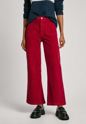 Pantaloni larghi in corduroy rosso con vita alta, tasche frontali e chiusura con bottone. Abbinati a scarpe con plateau nere.