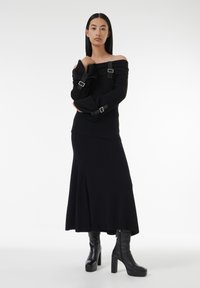 Pull noir à épaules dénudées en rib, avec des accents de boucle, associé à une longue jupe noire et des bottes à plateforme jusqu'aux genoux. Design minimaliste, texture lisse.