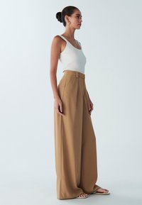 Beige vida byxor i mjukt tyg, kombinerade med en figurnära vit ribbad linne. Stilen kompletteras med enkla sandaler.