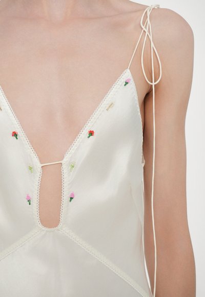 Zijden cami in off-white met een diepe V-hals, voorzien van bloemenborduursel in roze, rood en groen, afgewerkt met delicate kantafwerking en strikbandjes.