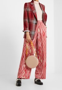 Rot kariertes Blazer, beiger Rollkragenpullover, gemusterte pinke weit geschnittene Hose, runde pinke Tasche mit Kette und schwarze Schuhe mit metallischen Akzenten.