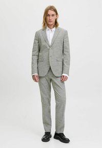 Traje gris claro hecho de tela texturizada, con una blazer de un solo botón, solapas acanaladas y pantalones de pierna recta. Combinado con una camisa blanca.