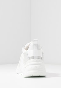 Baskets blanches et grises en mesh et daim, avec une semelle texturée, un col rembourré et une languette au talon.