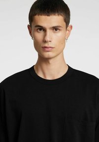 Svart bomulls-T-skjorte med rund hals og en liten lomme på venstre bryst. Myk tekstur med en avslappet passform.