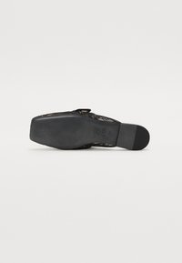Semelle plate de chaussure noire avec grip texturé, bout carré et marquages de taille, vue de dessous sur fond blanc.