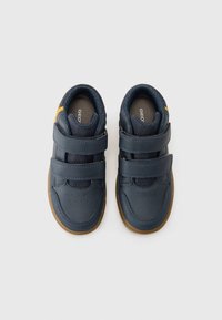 Granatowe sneakersy z podwójnymi rzepami, gumową podeszwą i perforowanym czubkiem dla lepszej oddychalności; z pomarańczowym akcentem w pobliżu pięty.