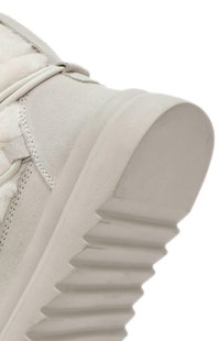 Zapatilla gris claro con material de ante, suela de goma texturizada y un tacón grueso y estriado. Se pueden ver los cordones y el interior suave.
