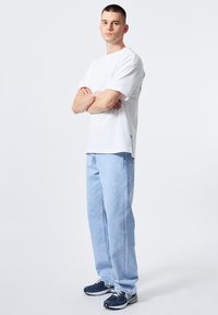 Camiseta blanca de manga corta, vaqueros holgados de color azul claro y zapatillas deportivas marinas. Diseño simple sin patrones ni logotipos visibles.