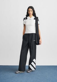 Άσπρο αθλητικό πουκάμισο με μαύρες λεπτομέρειες, μαύρο παντελόνι με φαρδιά μύτη και διαγώνιο λευκό σχέδιο, και ασημένια αθλητικά παπούτσια.