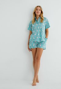 Conjunto de pijama turquesa que incluye una camisa de botones de manga corta y pantalones cortos a juego, adornados con patrones florales blancos y un ajuste relajado.