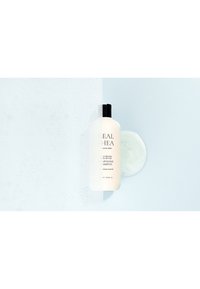Shampoo nutriente in una bottiglia di plastica bianca squeezable con un tappo nero. Texture in gel trasparente accanto, su uno sfondo azzurro chiaro.