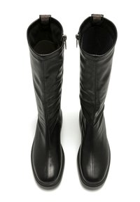 Bottes noires en cuir, montantes jusqu'au genou, avec une texture lisse, un design décontracté et des zips sur le côté, agrémentées de petits éléments décoratifs en haut.