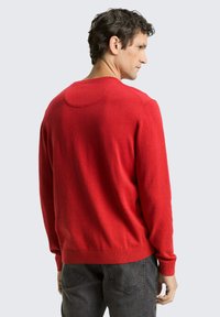 Maglione rosso in maglia con scollo rotondo e polsini a coste. Presenta una trama liscia e un design aderente, visto da dietro su uno sfondo chiaro.