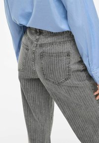 Jeans gris rayados con un corte ajustado, que presentan una cintura alta, dos bolsillos traseros y una textura deslavada. Combinados con una camisa de color azul claro.