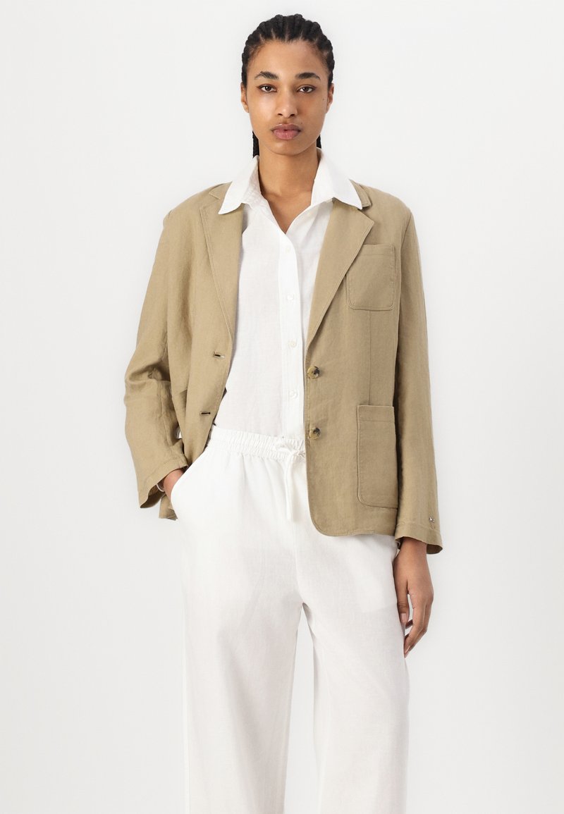 Lichtbeige linnen blazer met een relaxte pasvorm, twee voorkruiden en een omgeslagen kraag, gecombineerd met een witte overhemd en lichte broeken.