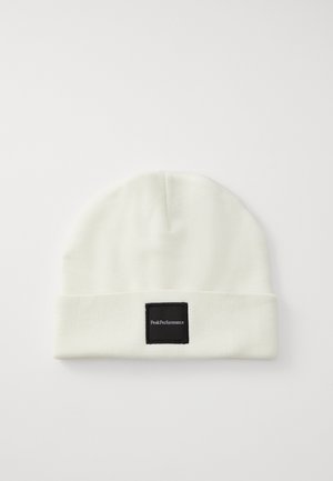 Witte gebreide beanie met een omgeslagen rand, voorzien van een vierkant zwart label met witte tekst, gemaakt van zacht materiaal voor warmte.