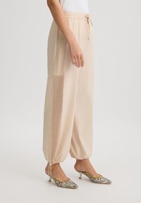 Pantaloni jogger leggeri beige con vita regolabile, dotati di un pannello in rete testurizzato sui lati e caviglie elastiche.