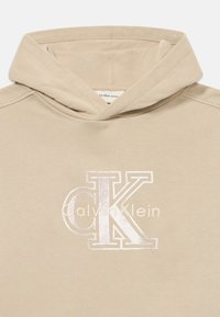 Sweatshirt bege com uma textura suave, apresentando um logo "CK" bordado em tom prateado e o texto "Calvin Klein" na parte da frente.