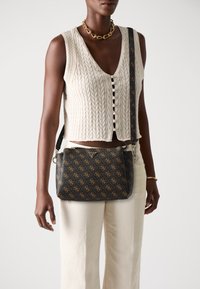 Sac à épaule noir à motifs avec des accents dorés et une bandoulière robuste, présentant un matériau lisse et une forme rectangulaire.