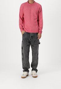 Pink knit sweater with ribbed neckline, paired with black distressed cargo pants featuring multiple pockets and white sneakers.