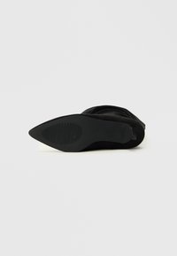 Bottine en suede noir avec un bout pointu et une semelle en caoutchouc texturé. Présente un léger talon et des détails piqués sur la tige.