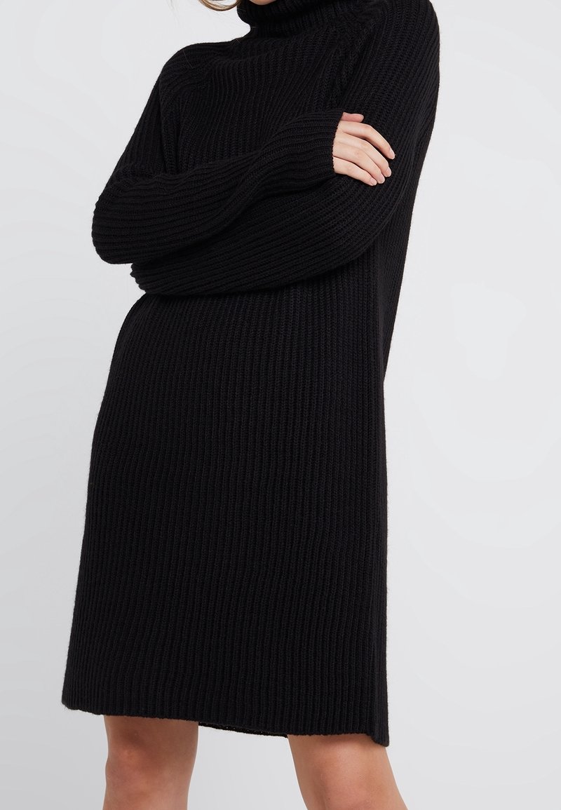 Czarna swetrowa sukienka z golfem, z długimi rękawami, luźnym krojem i lekko rozszerzanym dołem. Miękka faktura i średnia długość.
