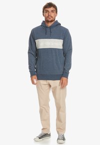 Sudadera azul marino con una banda horizontal gris que presenta texto de logo. Tejido suave, mangas largas, capucha ajustable con cordón y puños acanalados.