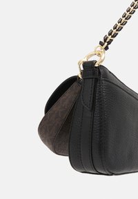 Sac à main en cuir noir grainé avec bandoulière chaîne dorée et vue latérale montrant des détails en couches et une pochette intérieure marron texturée.