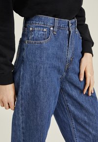 Högmidjade blå denimjeans med avslappnad passform, med guldfärgad sömnad, fem fickor och dragkedja. Släta, texturerade tyg.