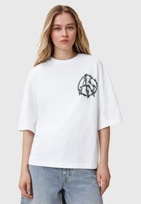 T-shirt bianco in cotone con vestibilità over, maniche corte e design grafico nero che presenta una catena intrecciata e lettere sulla parte anteriore.