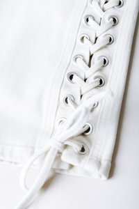 Λευκό ύφασμα με υφή διαθέτει κάθετο κορδόνι, ασημένια μεταλλικά γαντζάκια και δεμένο φιόγκο στο κάτω μέρος.