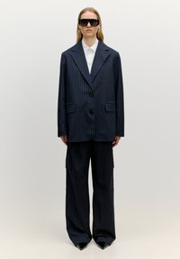 Marineblauer Nadelstreifenanzug mit maßgeschneidertem Blazer und weiten Cargo-Hosen. Enthält schwarze Knöpfe, strukturiertes Design und spitze Schuhe.