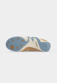 Semelle en caoutchouc d'une basket beige et bleue avec motifs de grip texturés et petits clous circulaires marron pour la traction.