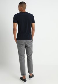 Tricou din bumbac de culoare bleumarin, pantaloni gri ușori cu manșete suflecate și adidași negri cu talpă albă, văzuți din spate.